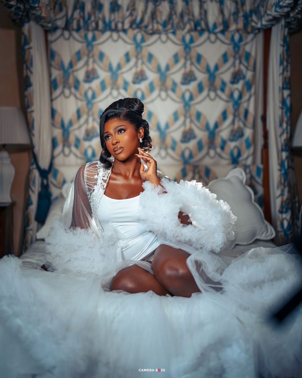 Elegant bridal portrait with flowing white tulle dress against blue and white damask wallpaper in romantic boudoir setting.