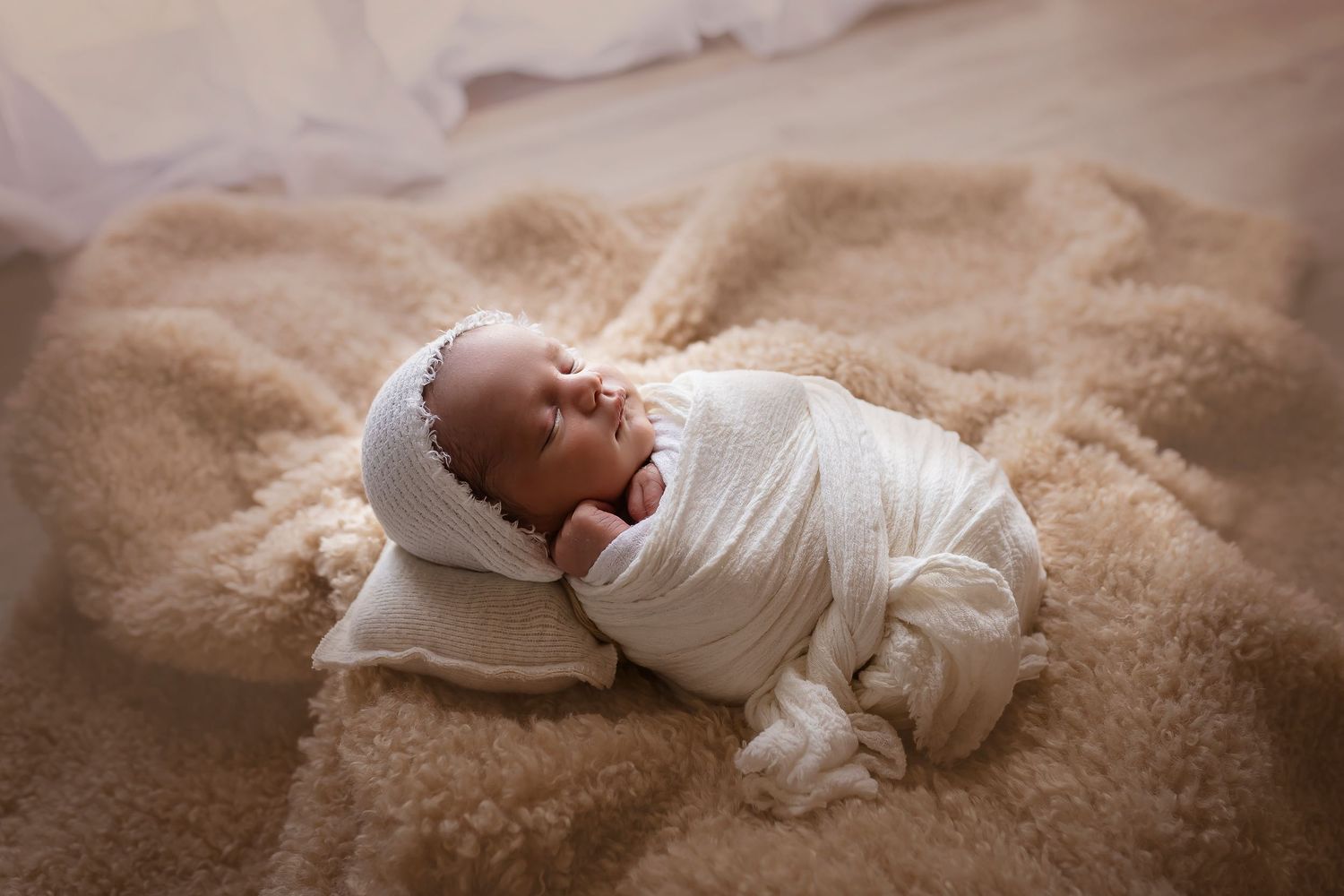 imagen tomada en contraluz bebe envuelto en blanco con manta que estira tiene gorrito blanco Fotografa de newborn