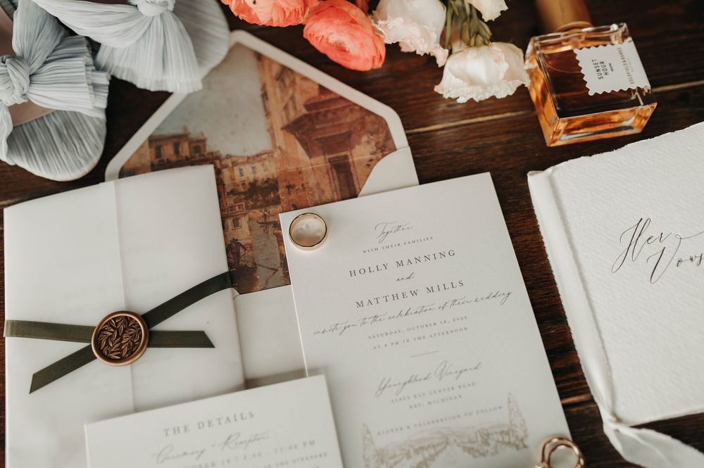 Elegant wedding invitation suite with wax seal, green ribbon, and floral envelope liner on a wooden surface.