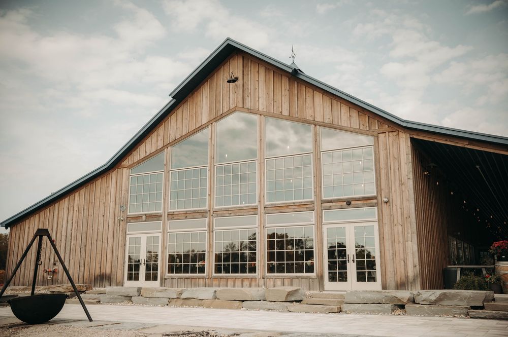 Rustic wooden barn wedding venue with large glass windows and industrial exterior under cloudy sky.