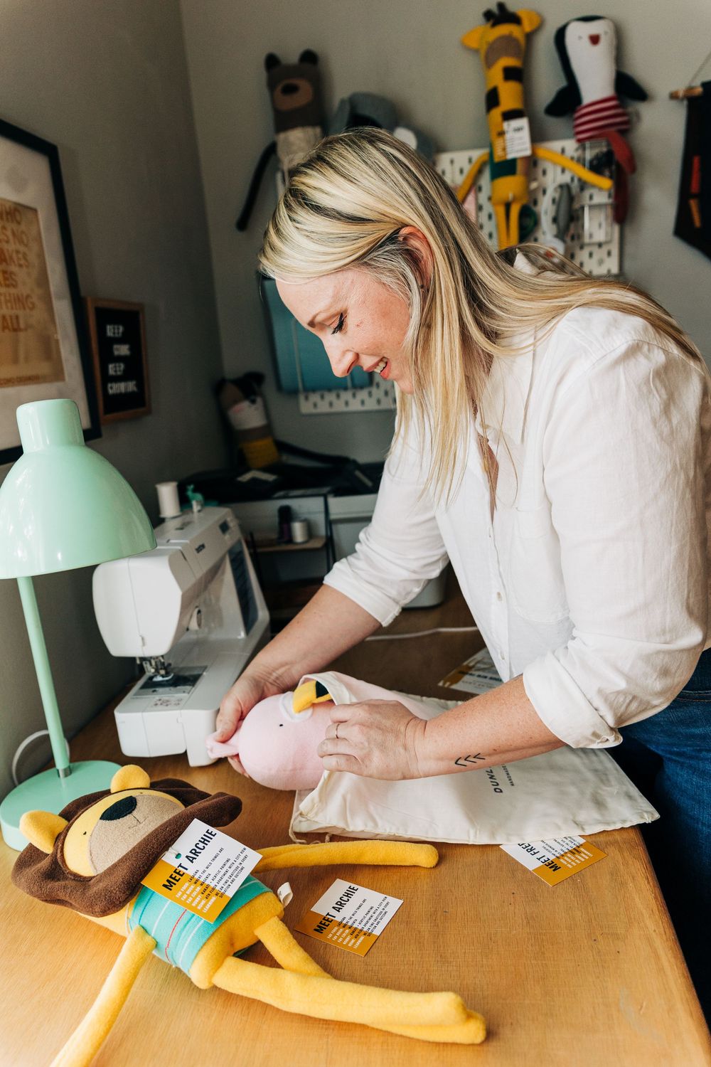 A seamstress works on a yellow fabric project at a wooden desk with sewing supplies and equipment.