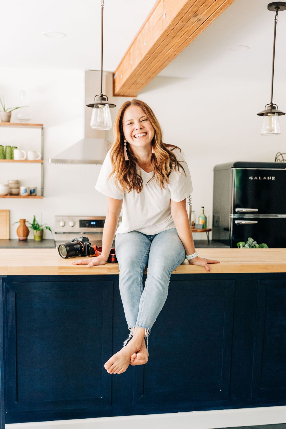 A woman sits on a counter smiling in a kitchen for headshot photos in Charlotte, NC.