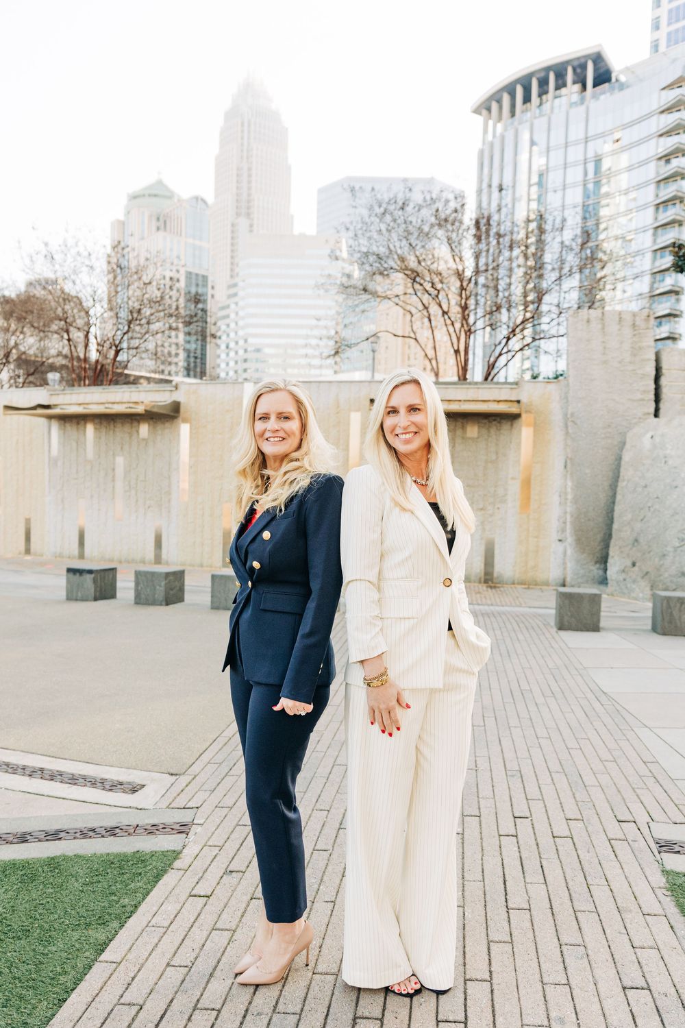 Two people in contrasting navy and cream outfits pose together on wooden decking in an urban setting.