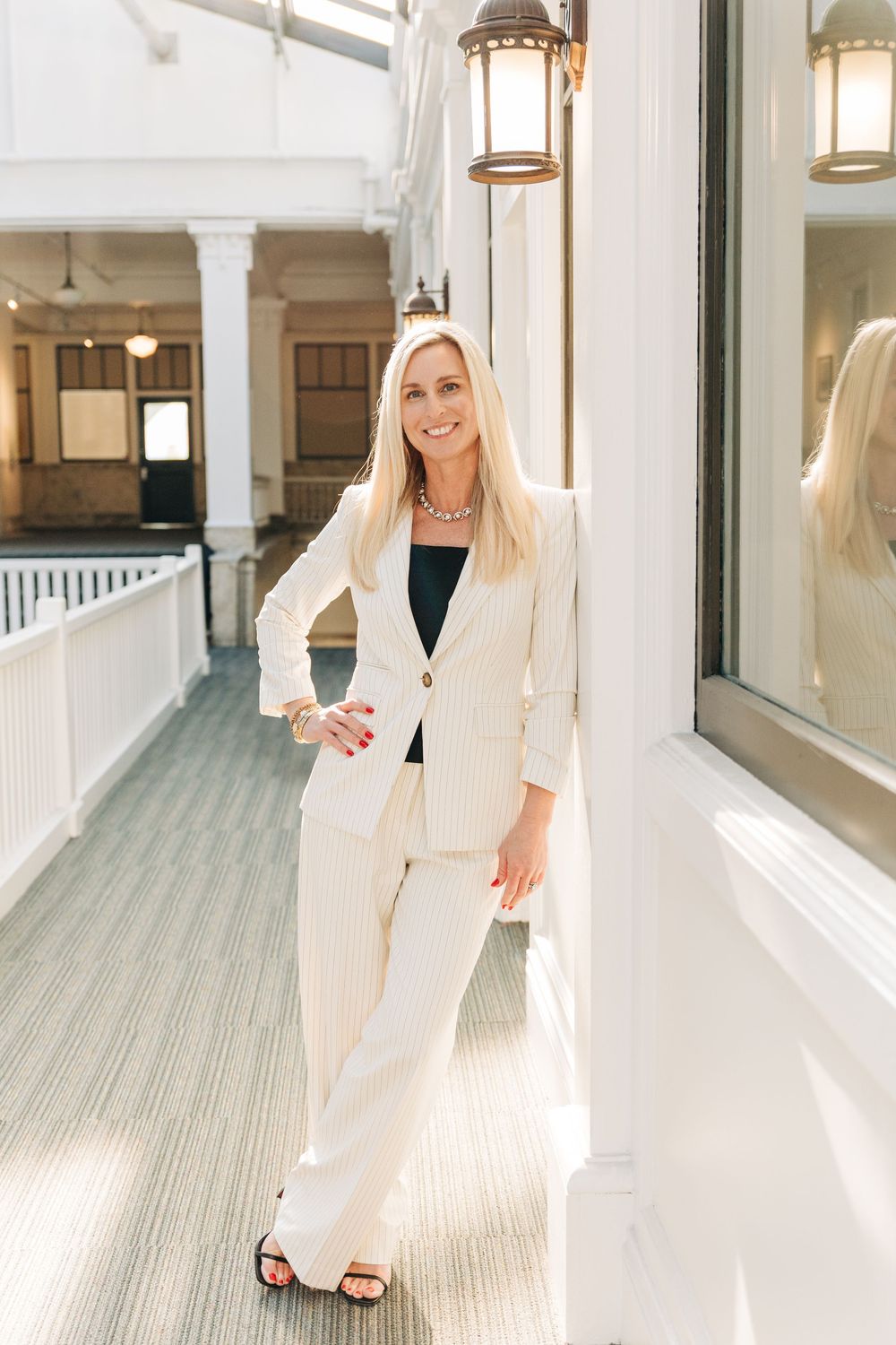 A bright white hallway photo showing a woman leaning in a white pantsuit for Charlotte headshot session.