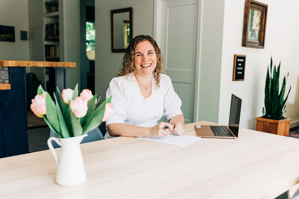 A bright modern workspace with a white desk, laptop, and tulips in a vase near a window.