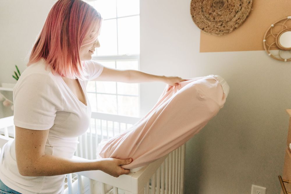 A woman puts a sheet on a baby crib mattress for branding photos in Charlotte, NC.