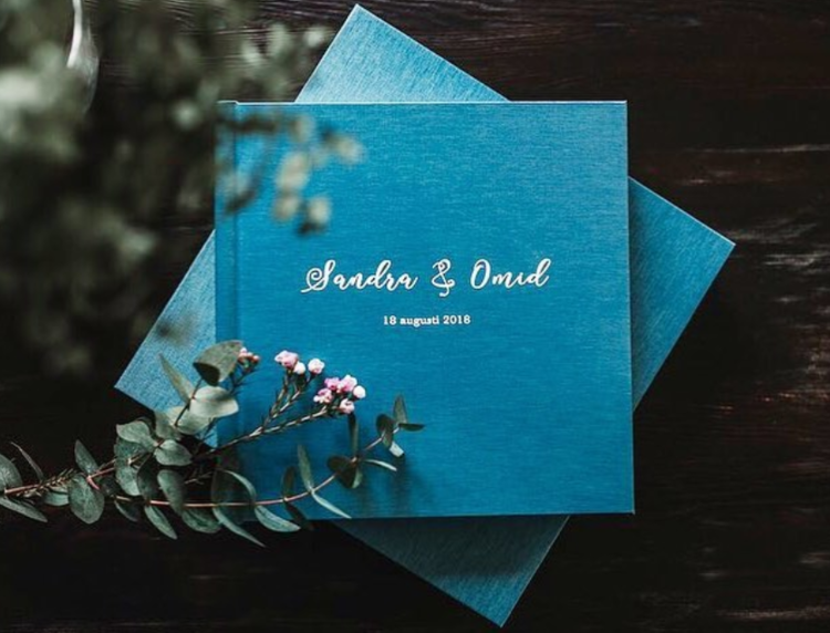 Turquoise wedding album with names and date surrounded by eucalyptus leaves.