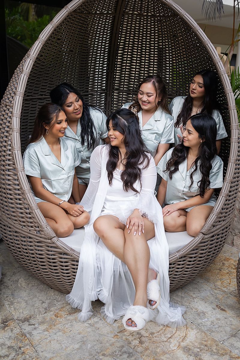 A group in matching white outfits sits together in a large woven egg-shaped chair during a special occasion photoshoot.