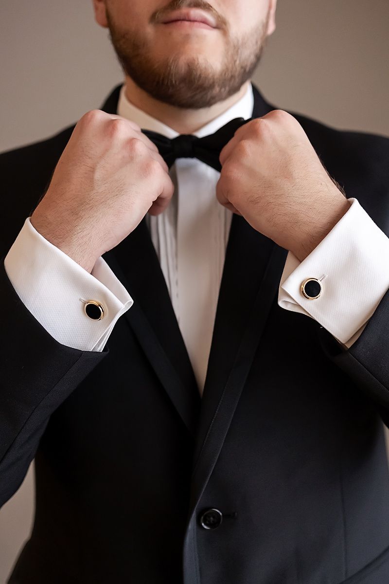 Close-up of hands adjusting black bow tie and cufflinks on formal tuxedo with white dress shirt.