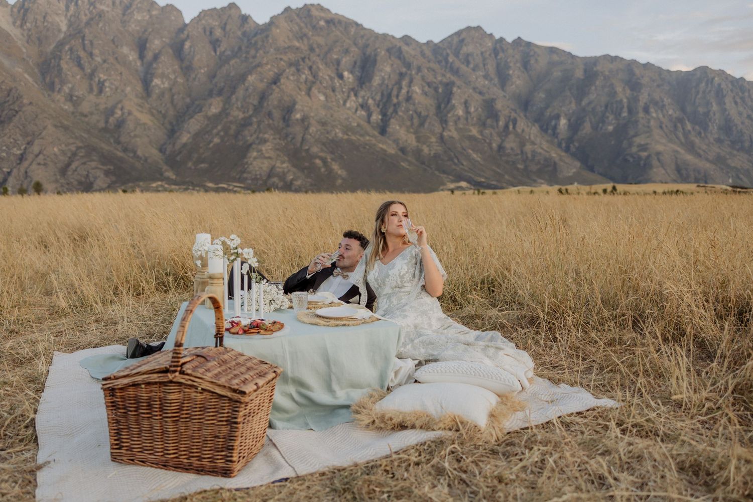 Picnic setup with basket and blanket in mountain meadow at sunset.