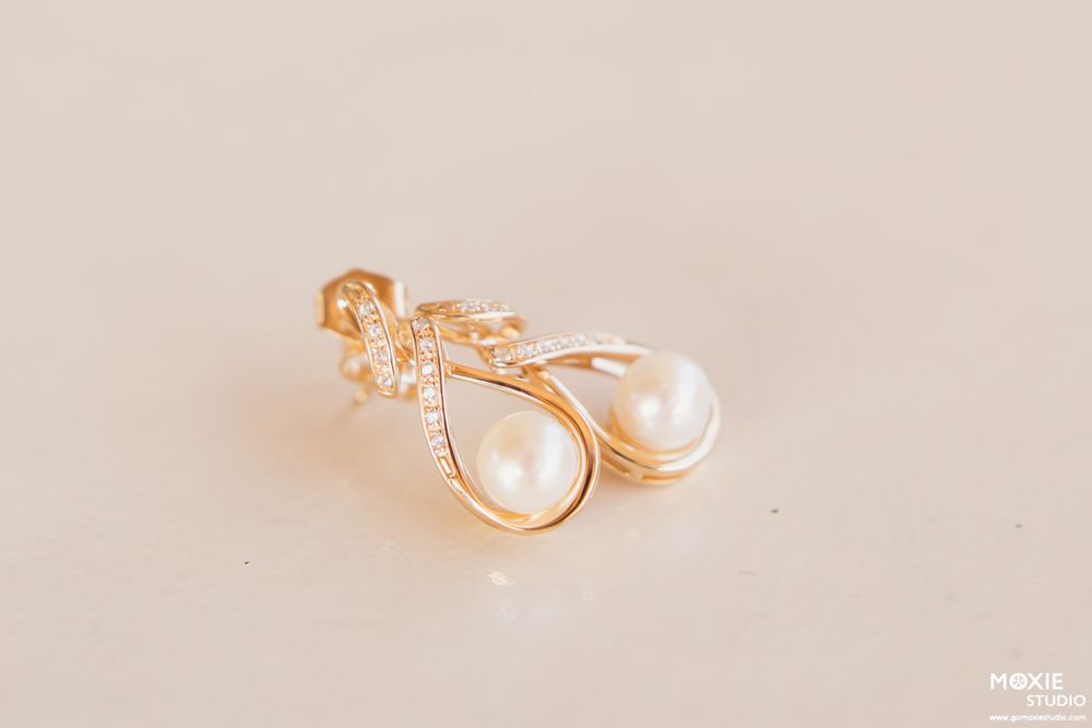 Delicate rose gold jewelry pieces including rings and pearl earrings arranged on a light beige background.
