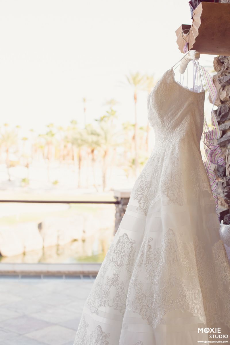 Elegant white wedding dresses with intricate lace details displayed on hangers in a bridal boutique.