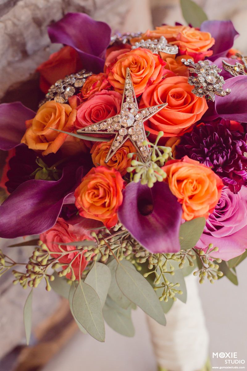 Close-up view of vibrant orange roses and purple flowers with crystal embellishments in a wedding bouquet arrangement.