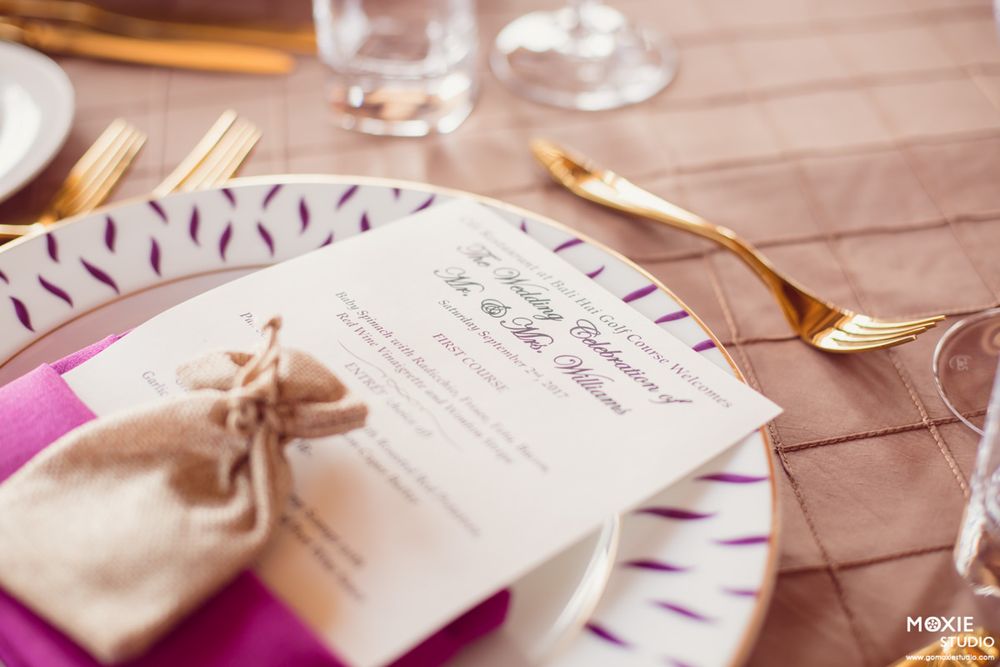 Wedding reception table settings with pink accents, gold cutlery, and menu cards tied with ribbon.