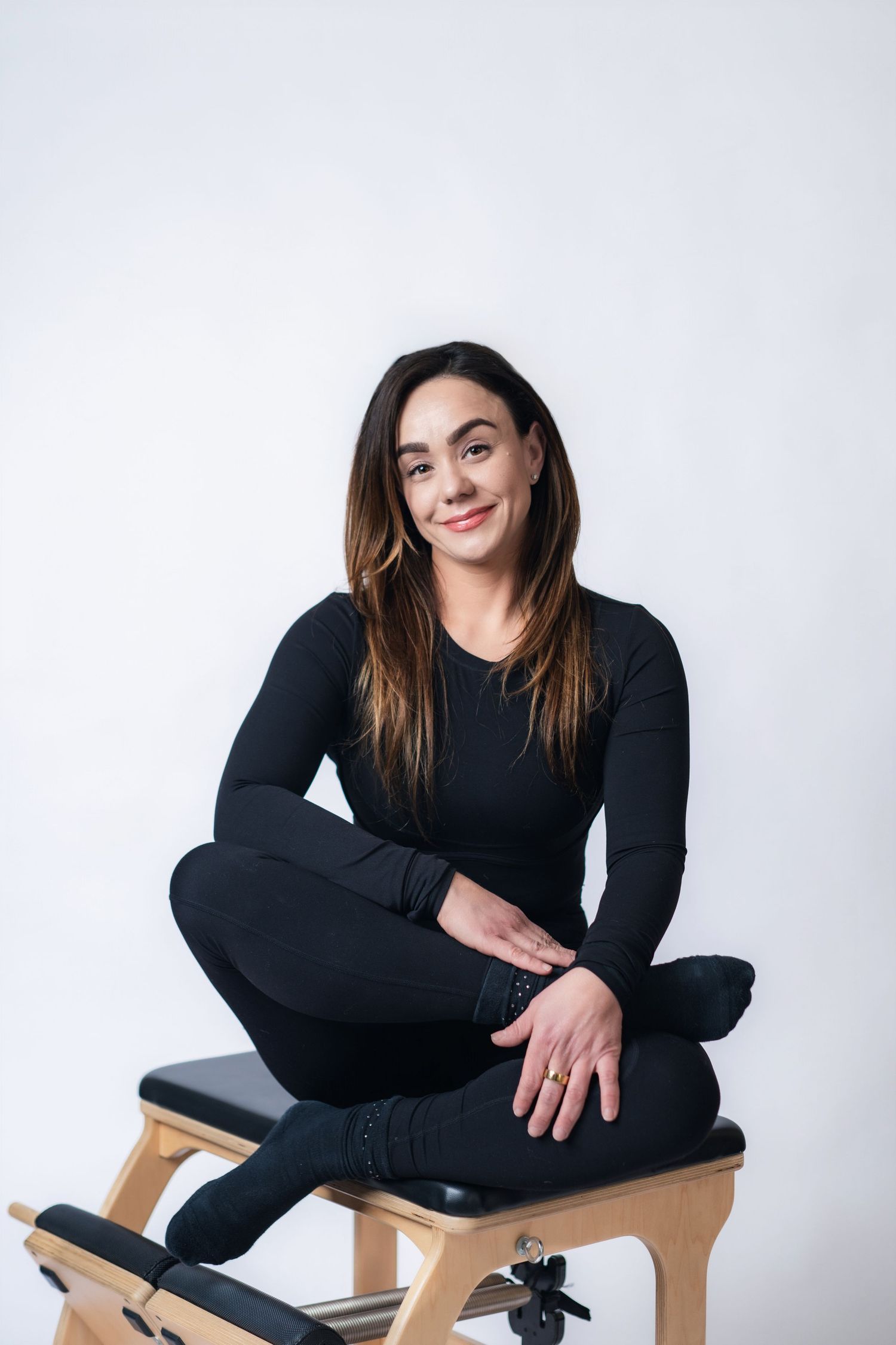 Person wearing all black sits cross-legged on wooden stool against white background in three different poses.