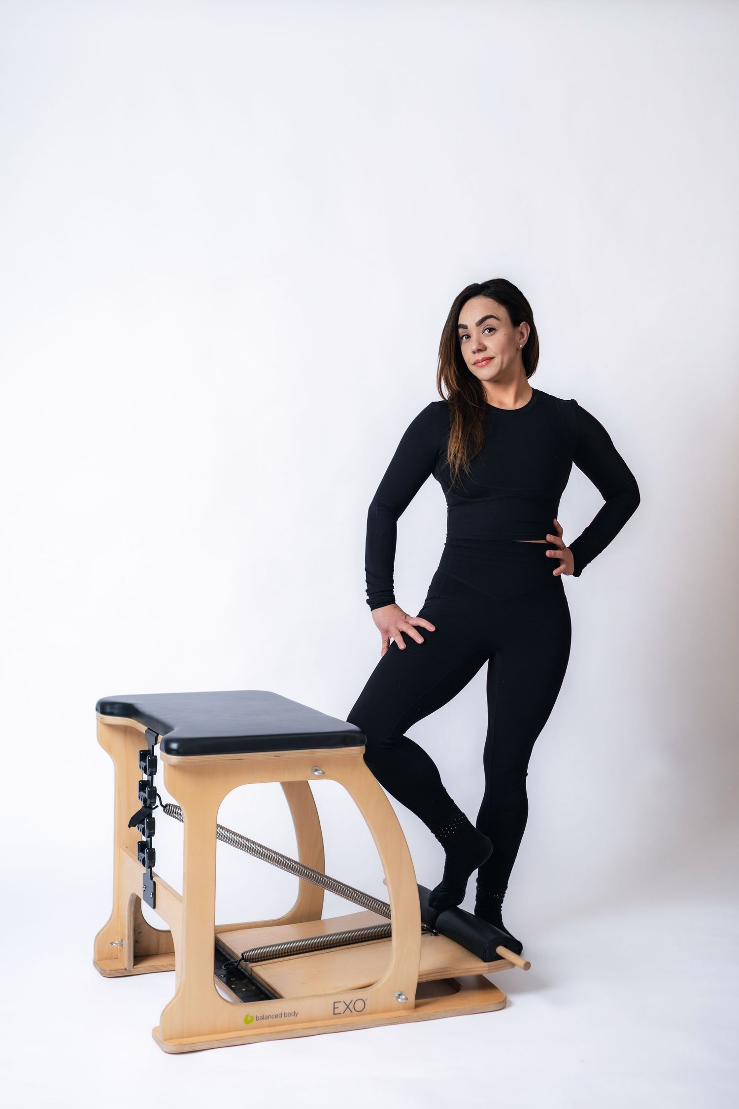 A person in black attire demonstrates different poses on a wooden ergonomic furniture piece against a white backdrop.