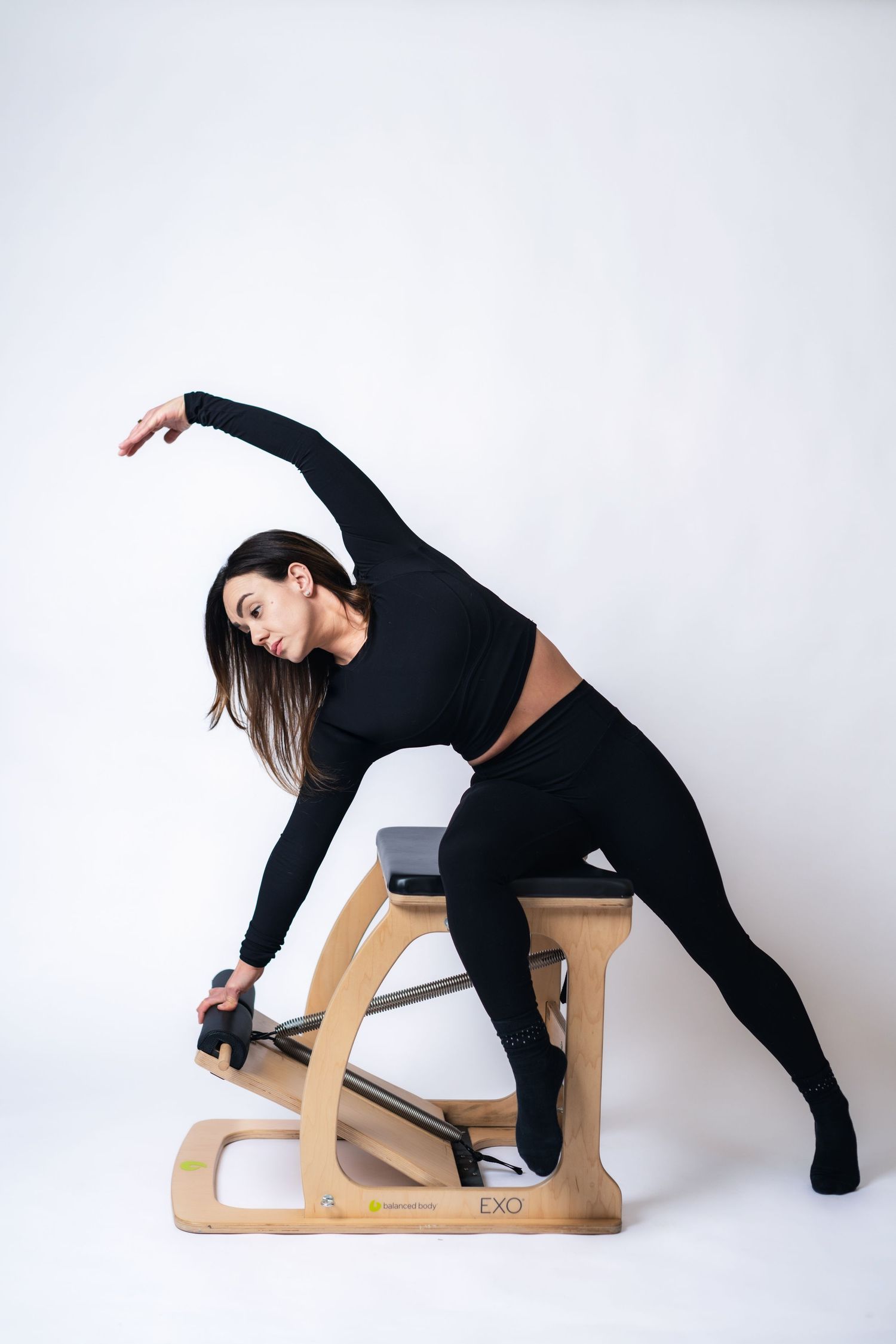 A person demonstrates stretching poses on a wooden yoga prop against a white background.