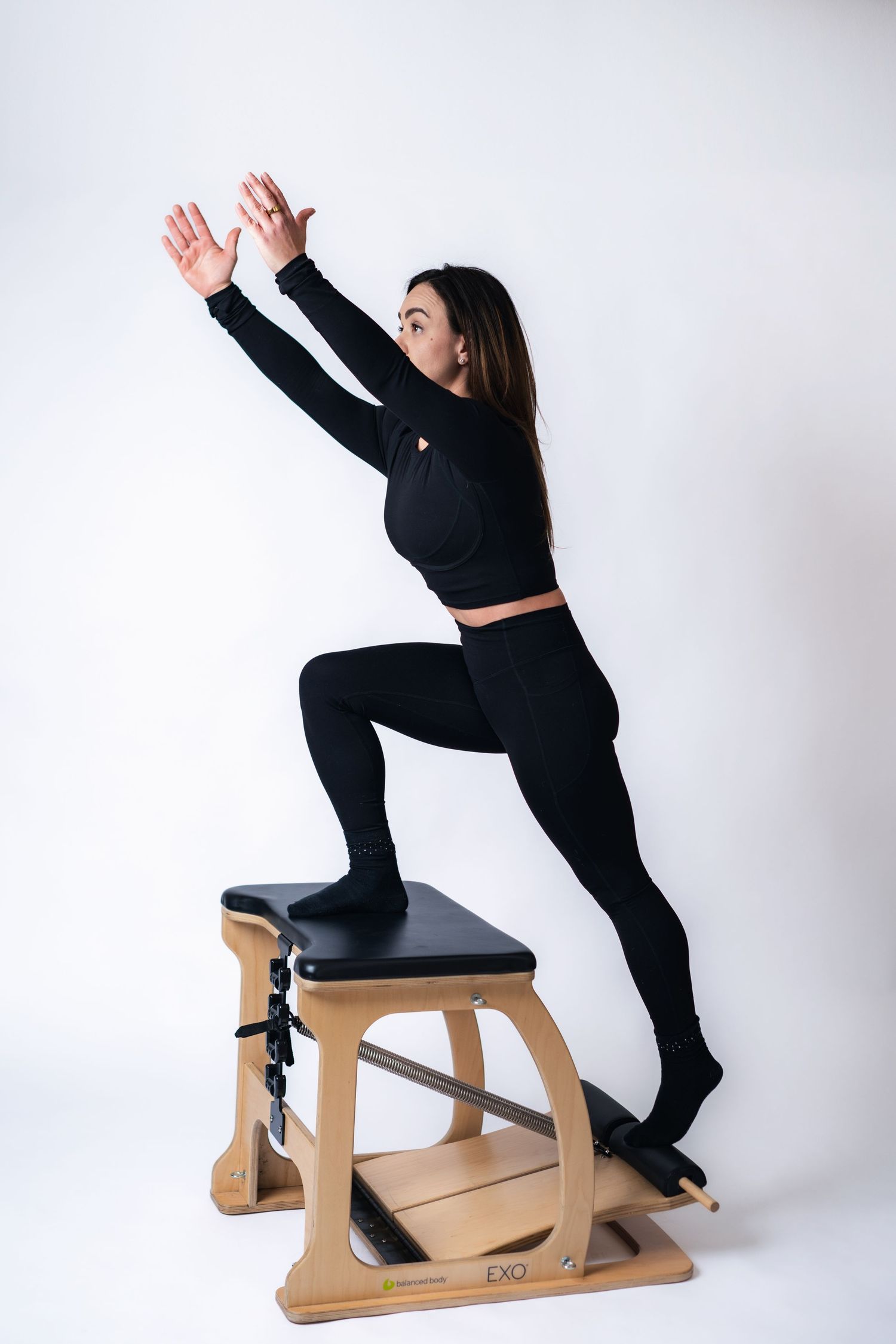 Person in black athletic wear demonstrates stretching exercises using a wooden exercise bench against white background.