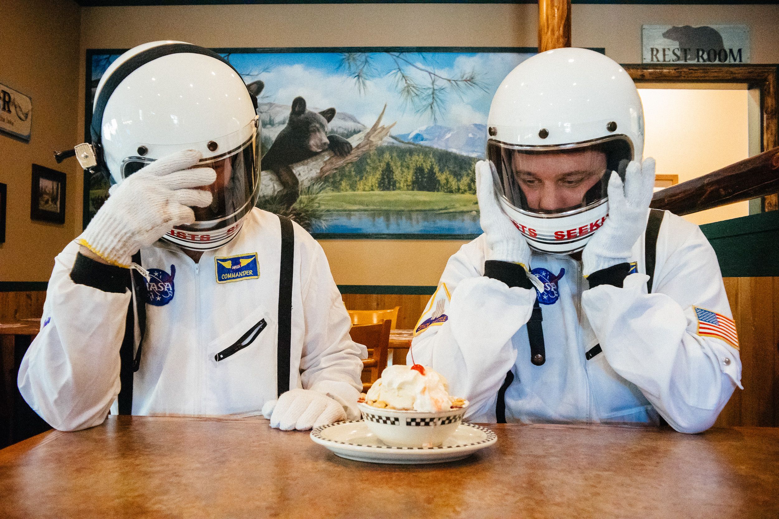 A person in a white racing helmet and protective gear sits at a table in what appears to be a dining area.