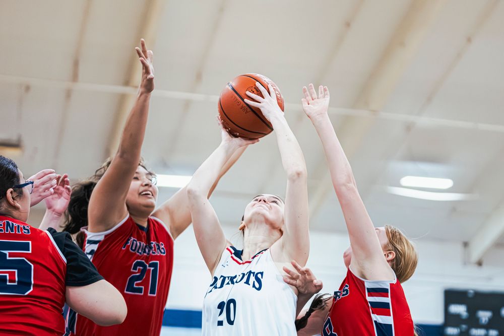 Girls Basketball player reaching up with ball to get a basket