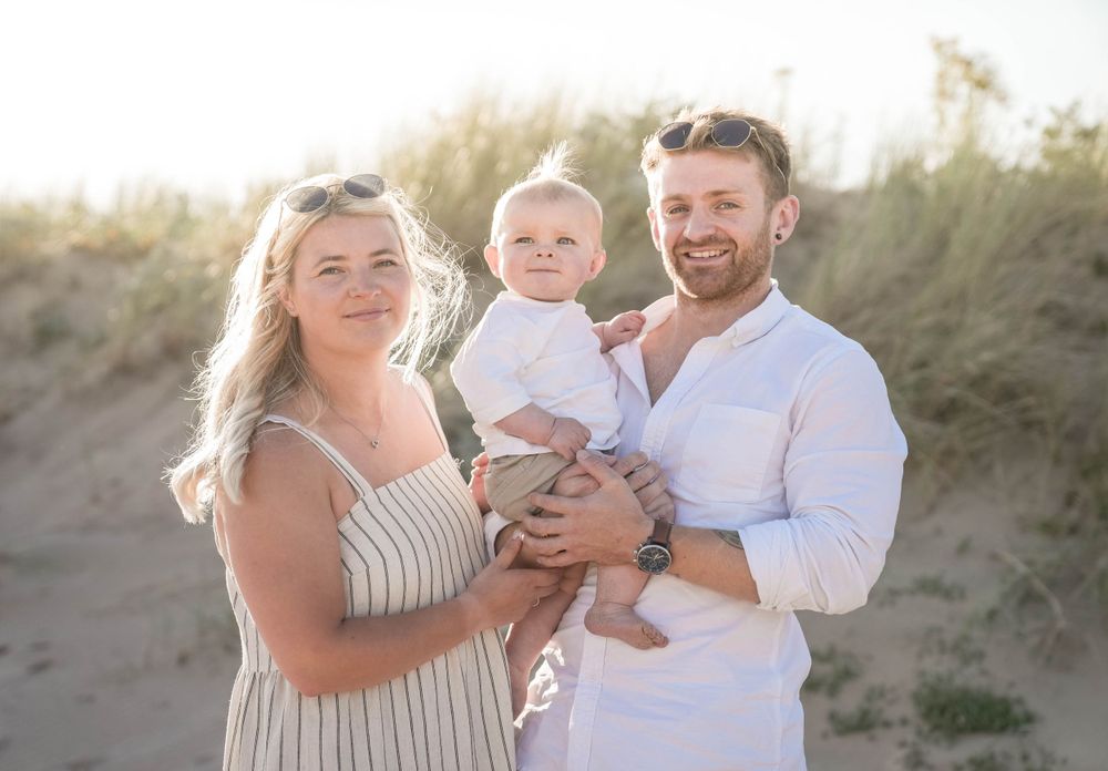 Happy family embracing on beach dunes during golden hour.