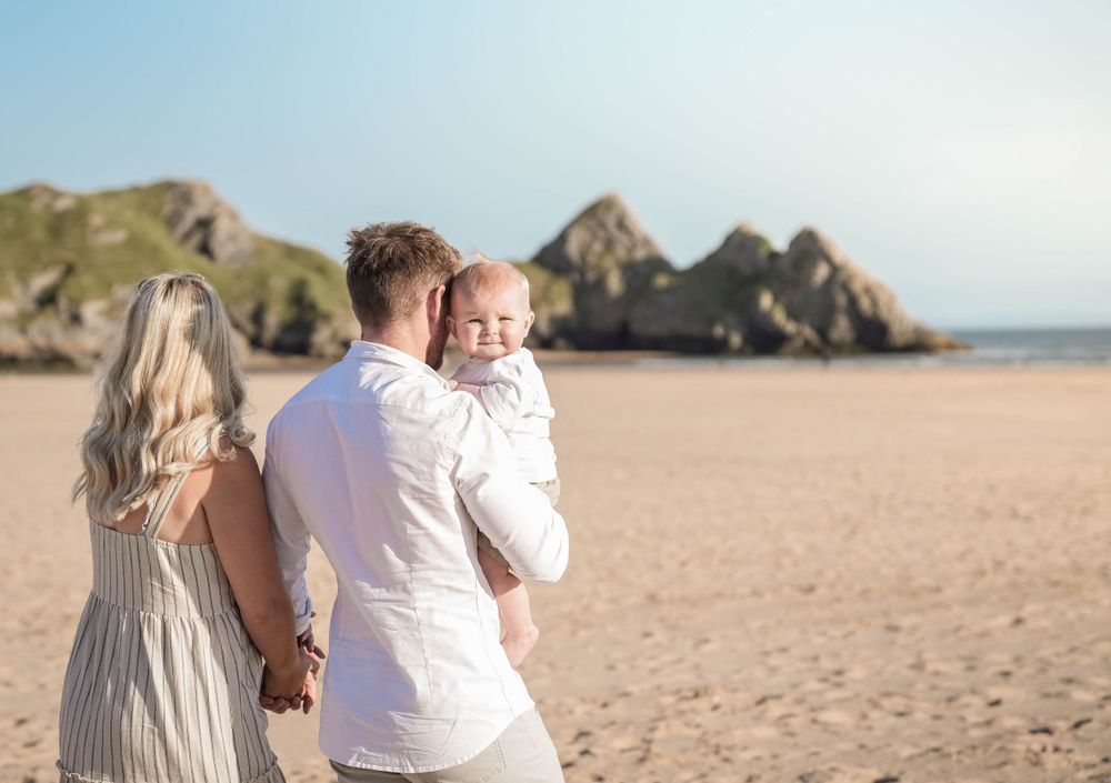 A family enjoying a sunny day together at a scenic beach with dramatic coastal cliffs in the background.