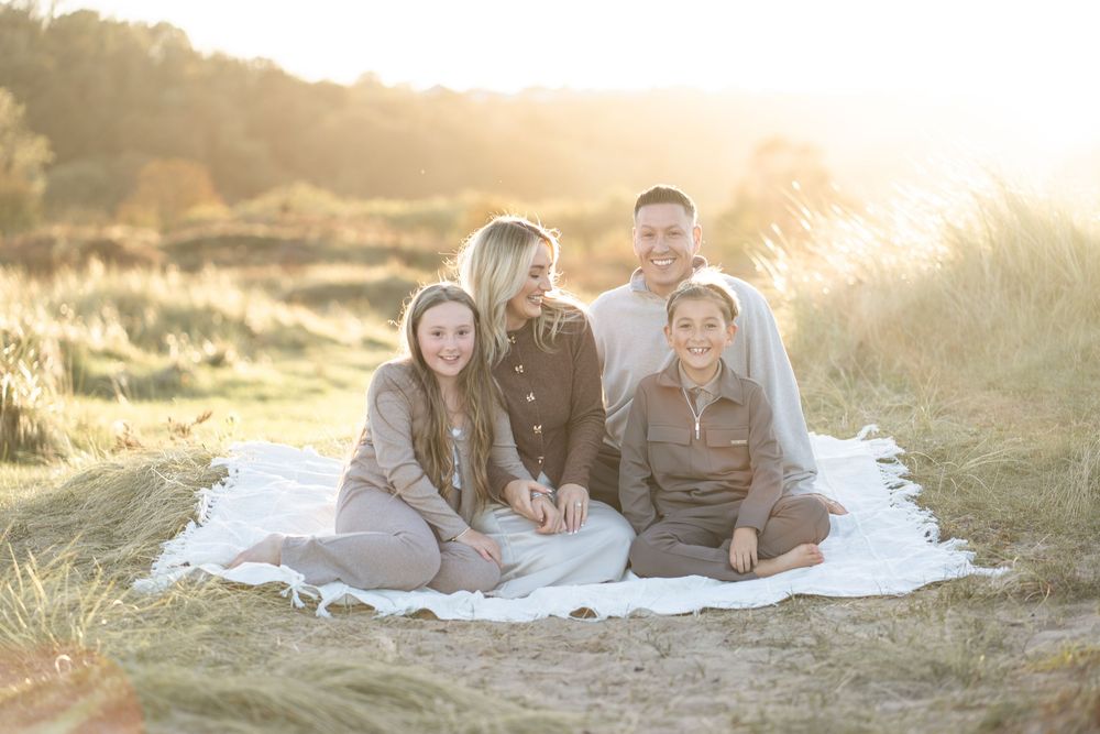 A series of outdoor family portraits taken at golden hour with people lying on white blankets in a grassy field.