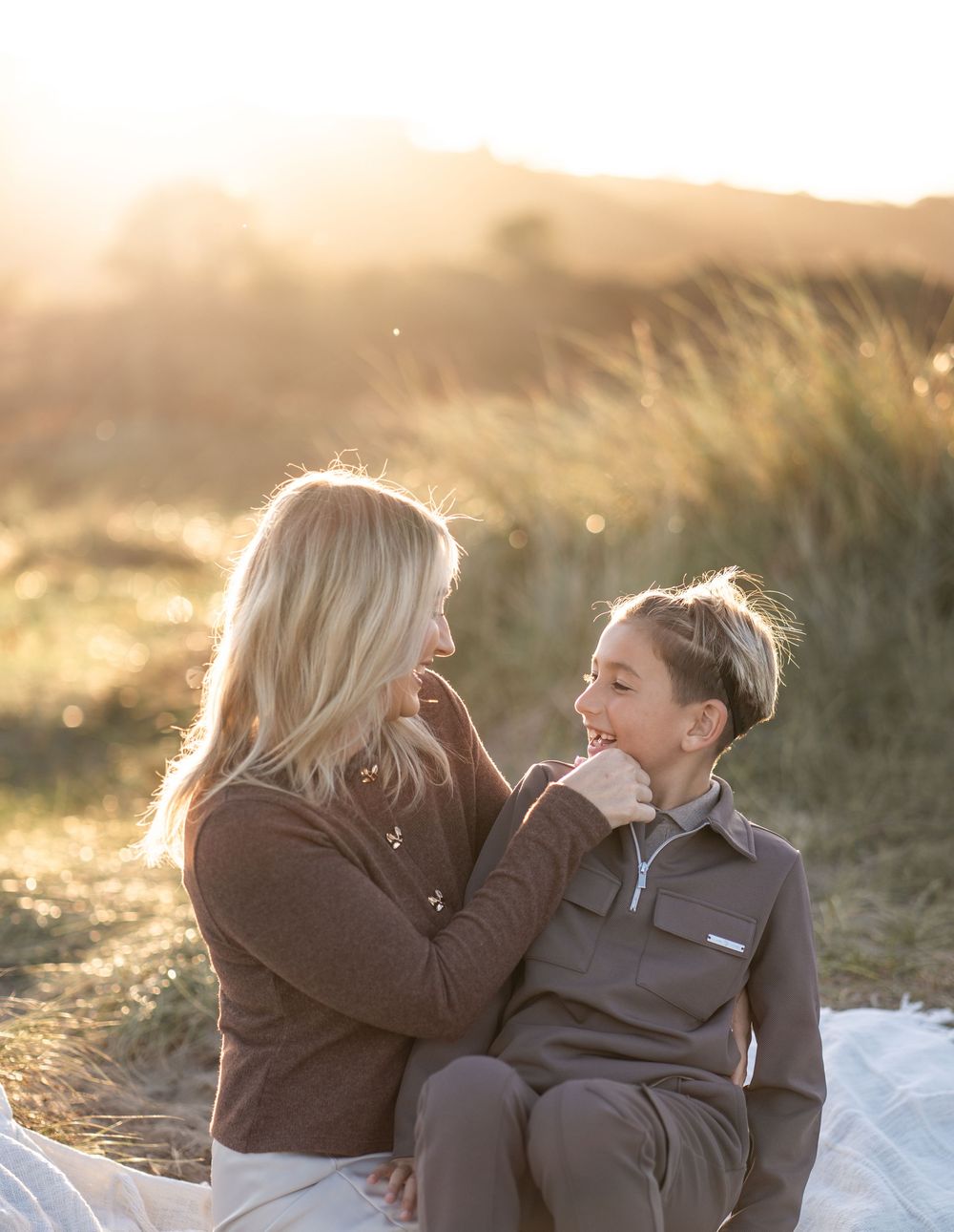Two people share a tender moment in golden sunlight against a natural outdoor backdrop during sunset.