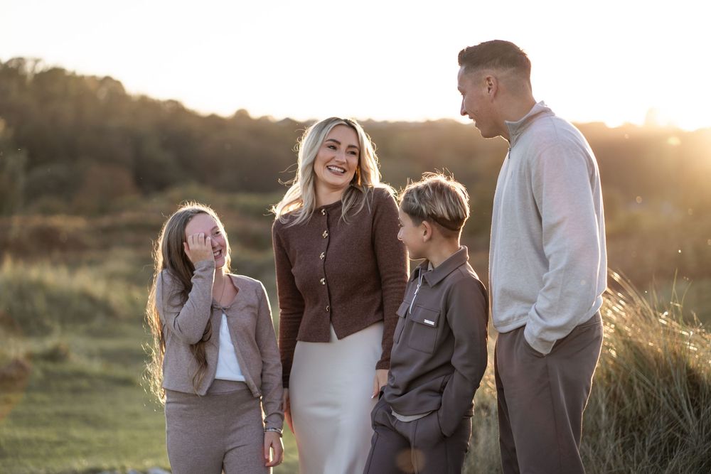 A joyful family of four sharing laughter together outdoors during sunset.