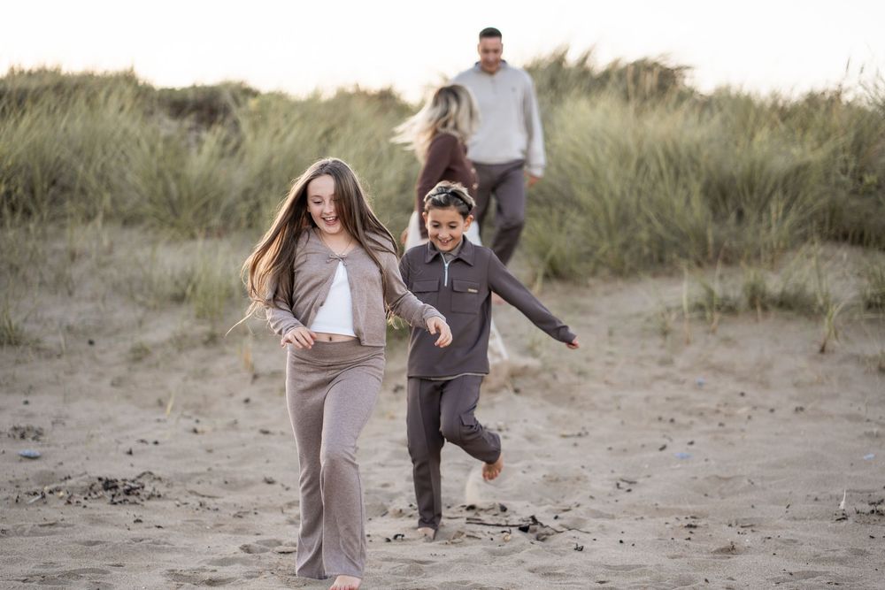 A couple walks playfully along sandy beach dunes during a romantic photoshoot at sunset.