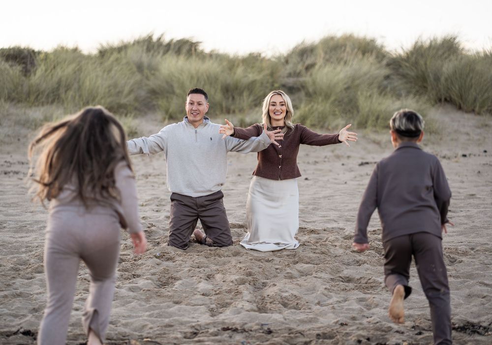 Family walking together on a sandy beach during sunset wearing coordinated neutral tones.