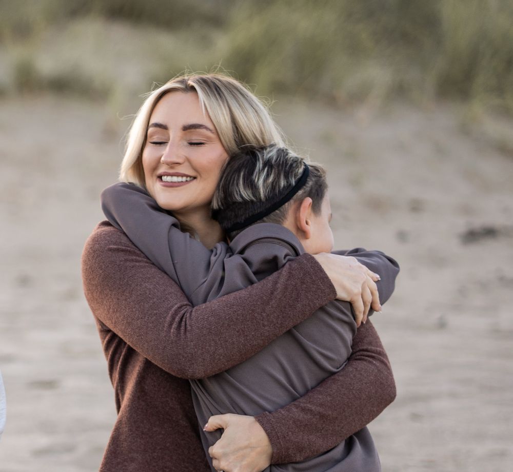 Two people share a warm embrace on a sandy beach during what appears to be a romantic moment.