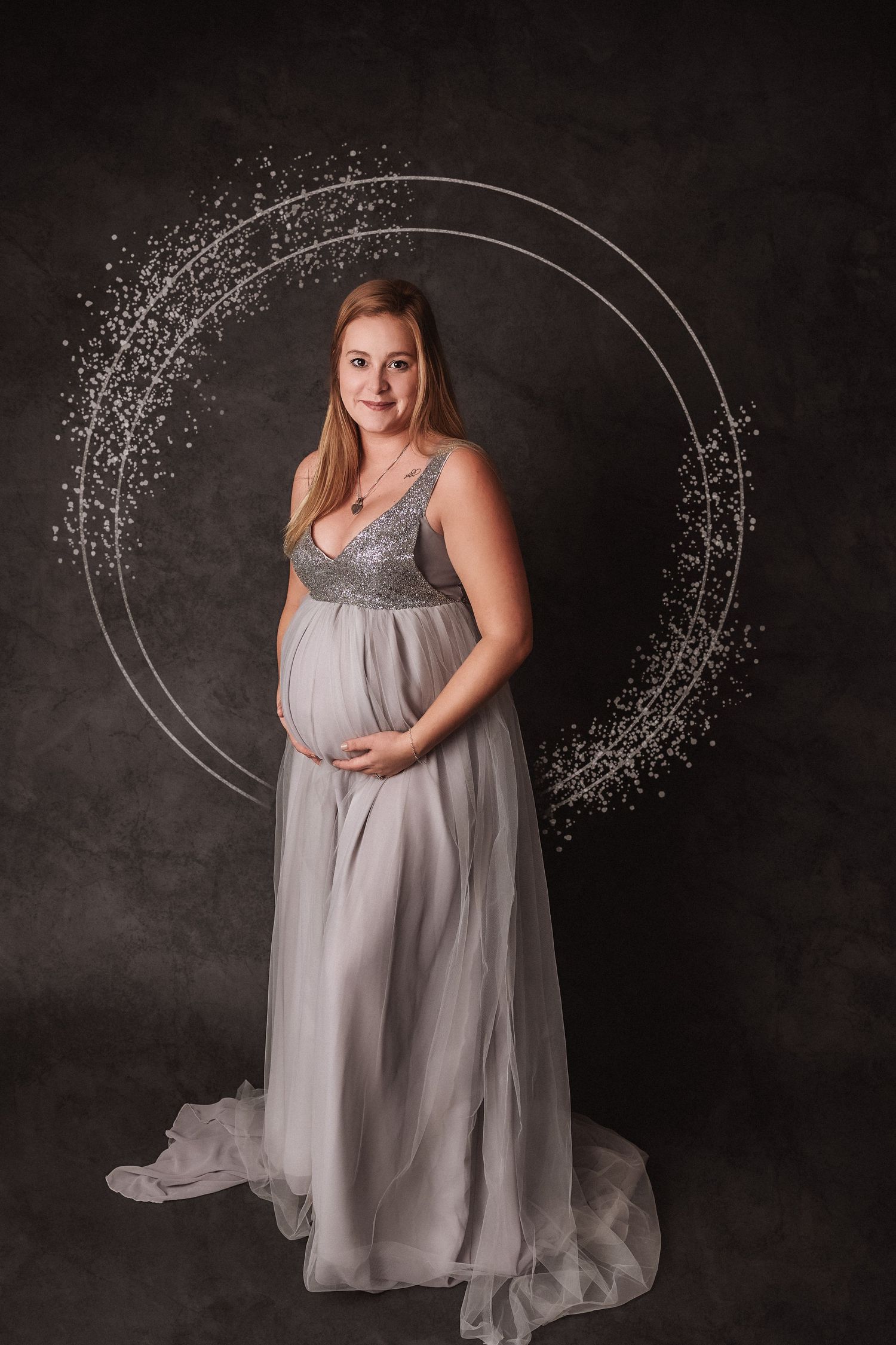 A maternity portrait features a flowing gray gown with a sequined bodice against a dark background with glowing circular elements.