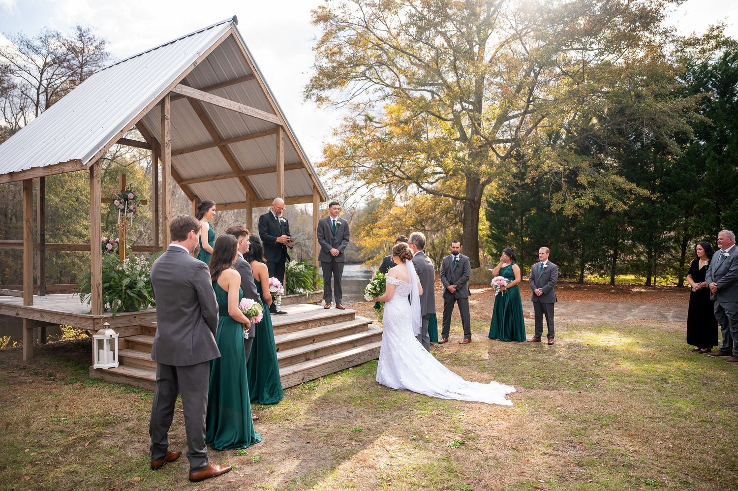 Panoramic view of outdoor wedding ceremony setup with guests and natural fall scenery.