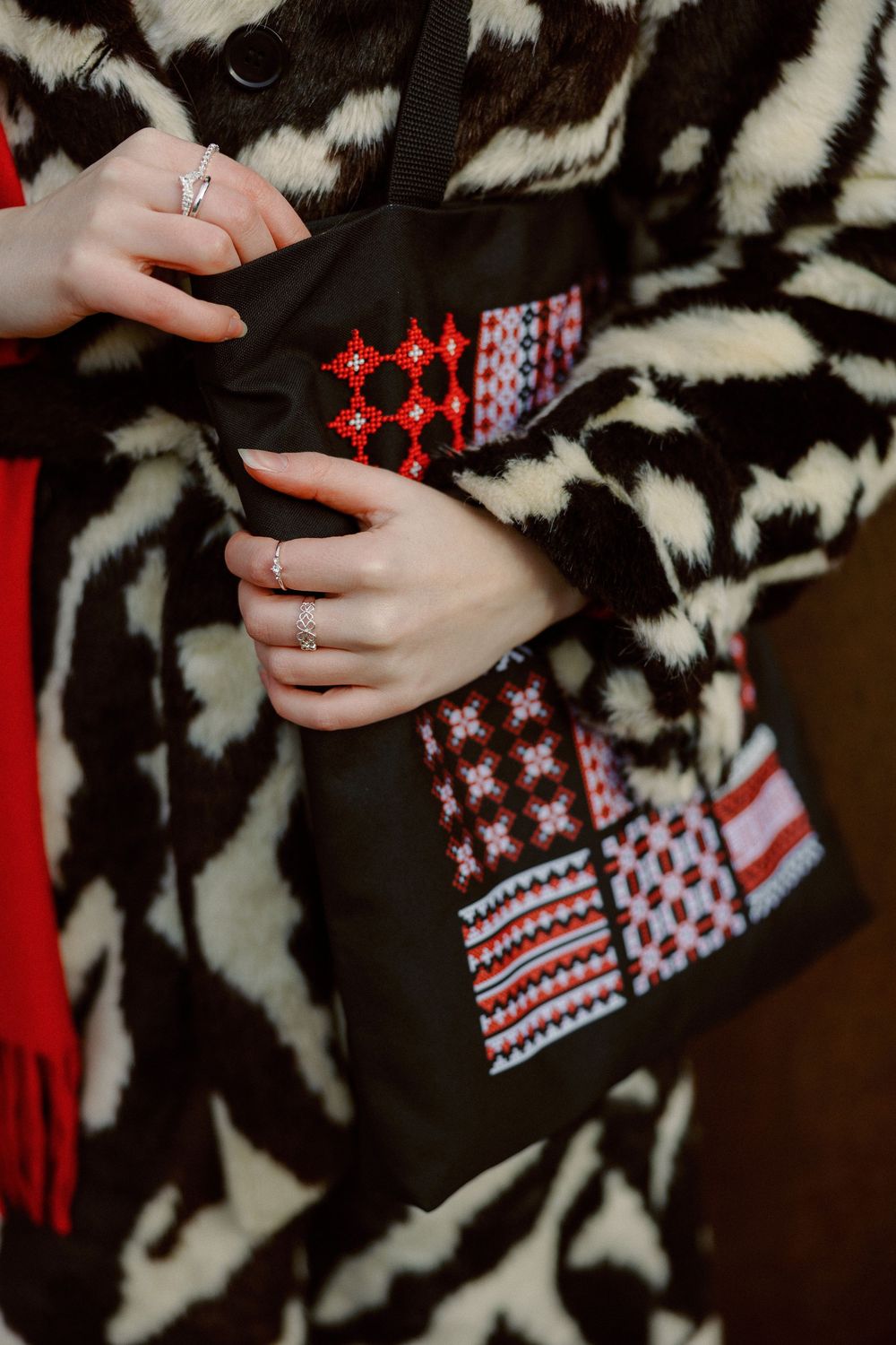 Hands with rings hold a black garment with red and white Nordic-style embroidered pattern against zebra print background.