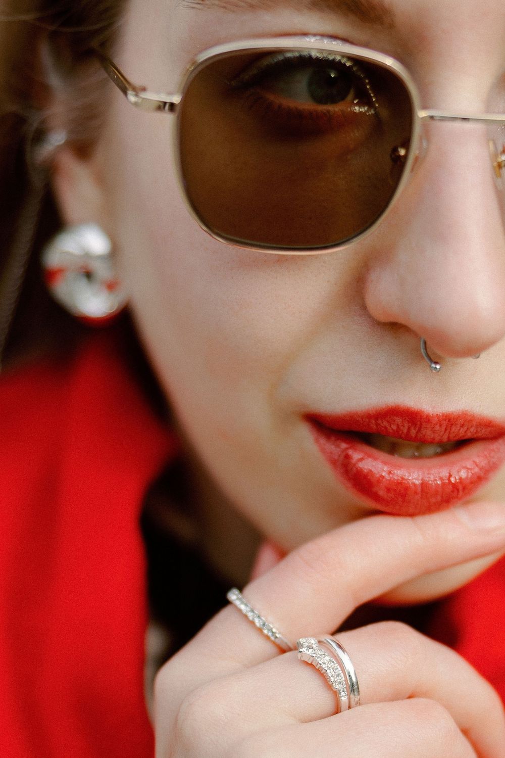Close-up of sunglasses and red lipstick with a diamond engagement ring on display against a red background.