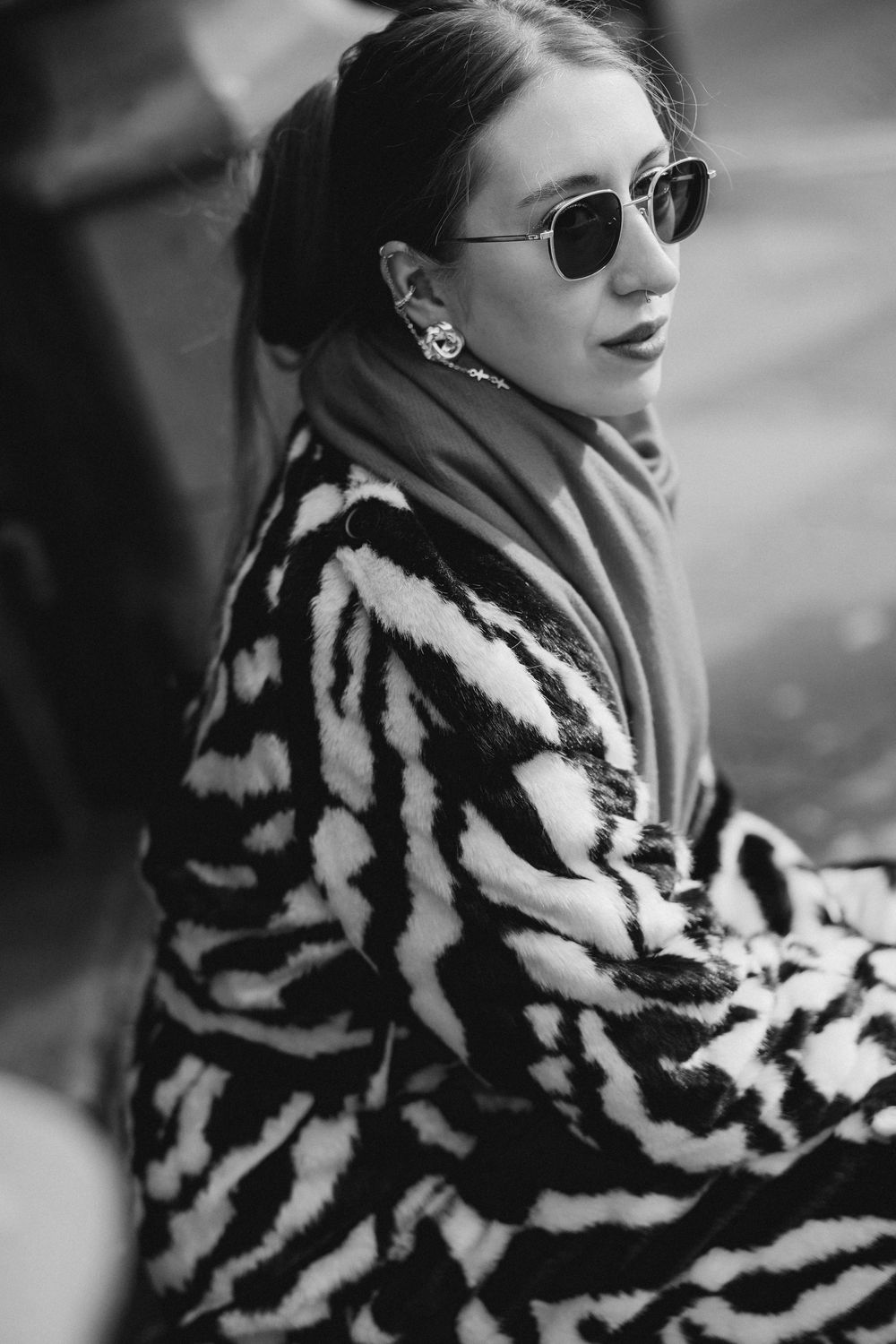 A black and white photo series showing someone in a dramatic zebra-striped fur coat and sunglasses posing outdoors.