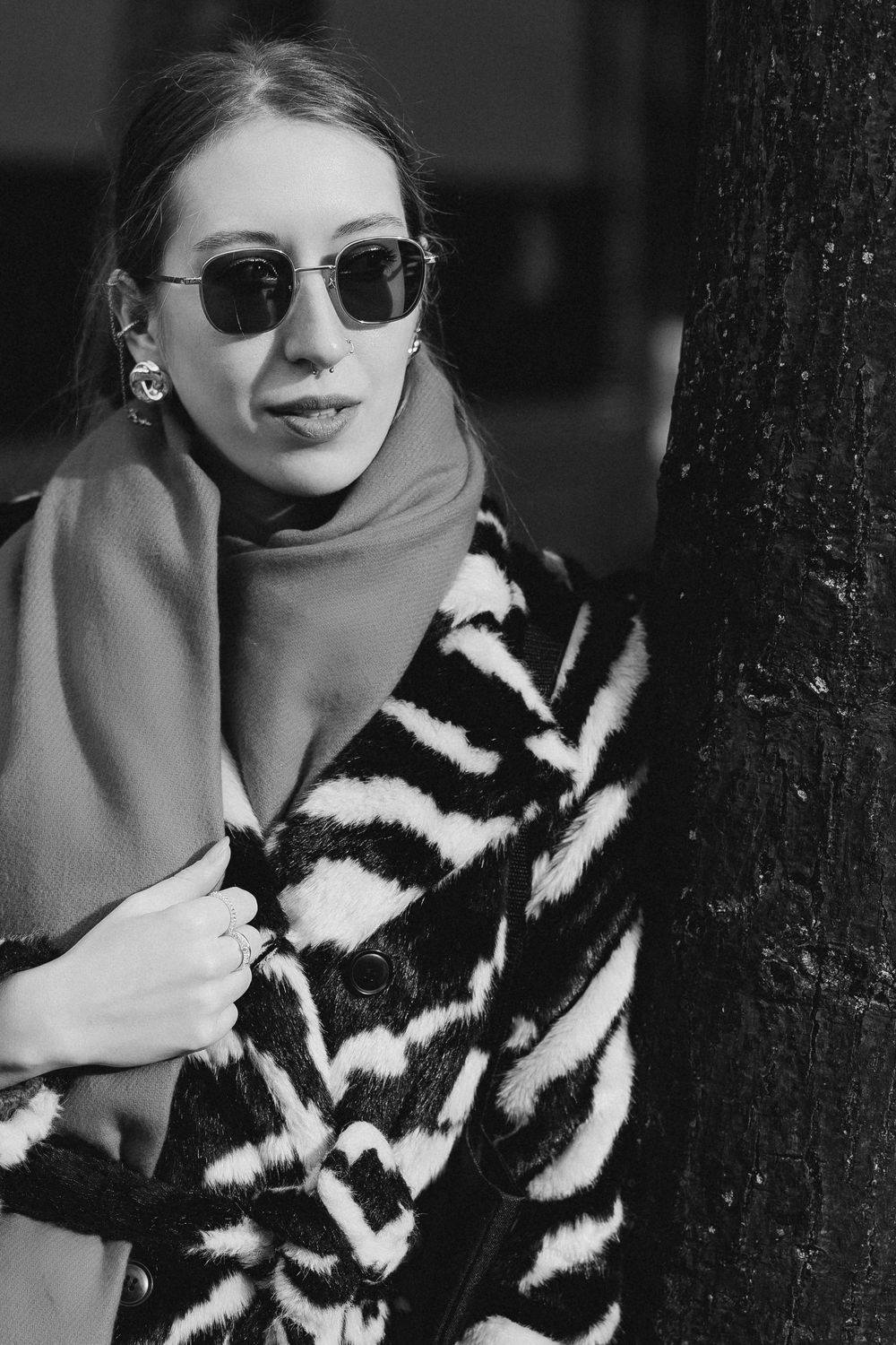 A black and white fashion photo of someone wearing a striped fur coat and sunglasses against a dark background.