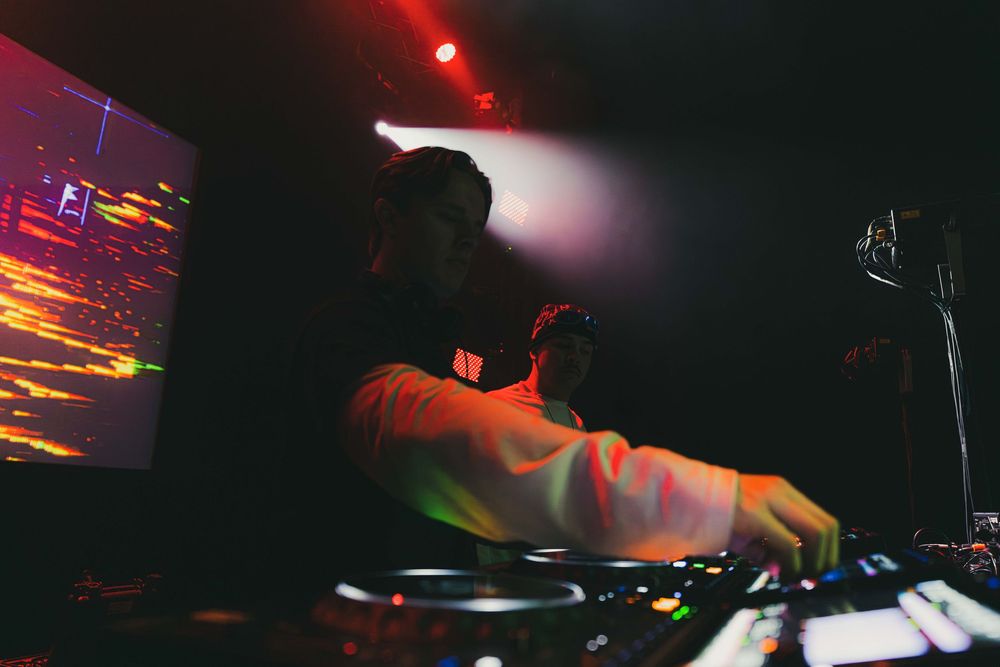 Red stage lighting creates a dramatic atmosphere over DJ equipment at a nightclub performance.