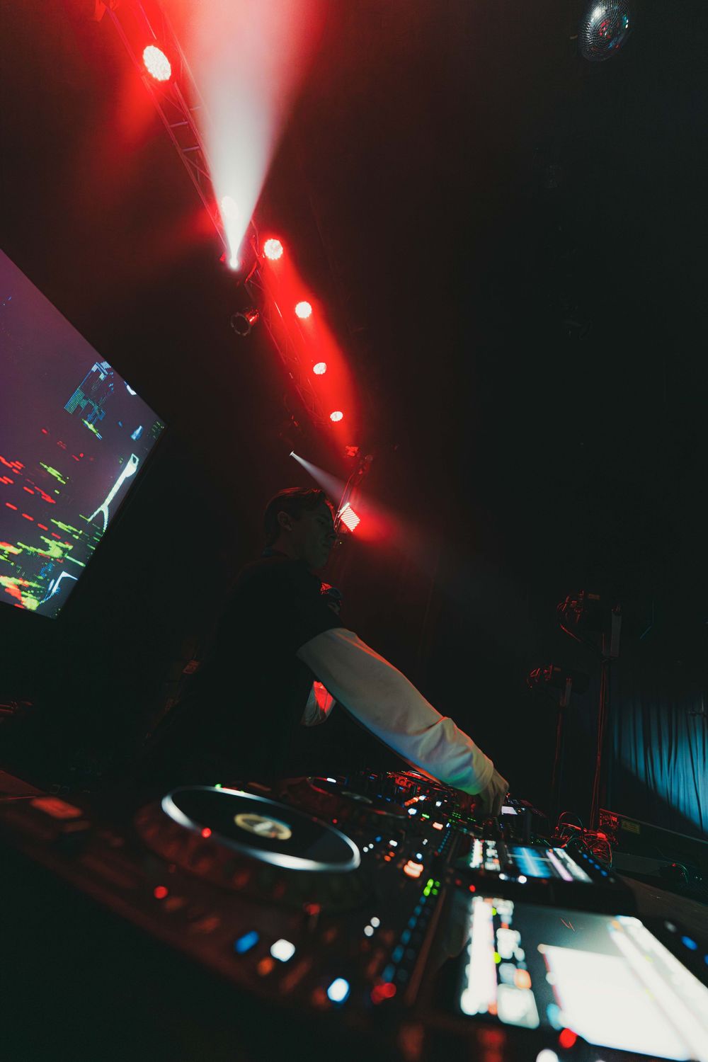 DJ equipment and turntables illuminated by red lights in a dark nightclub setting with glowing blue accents.