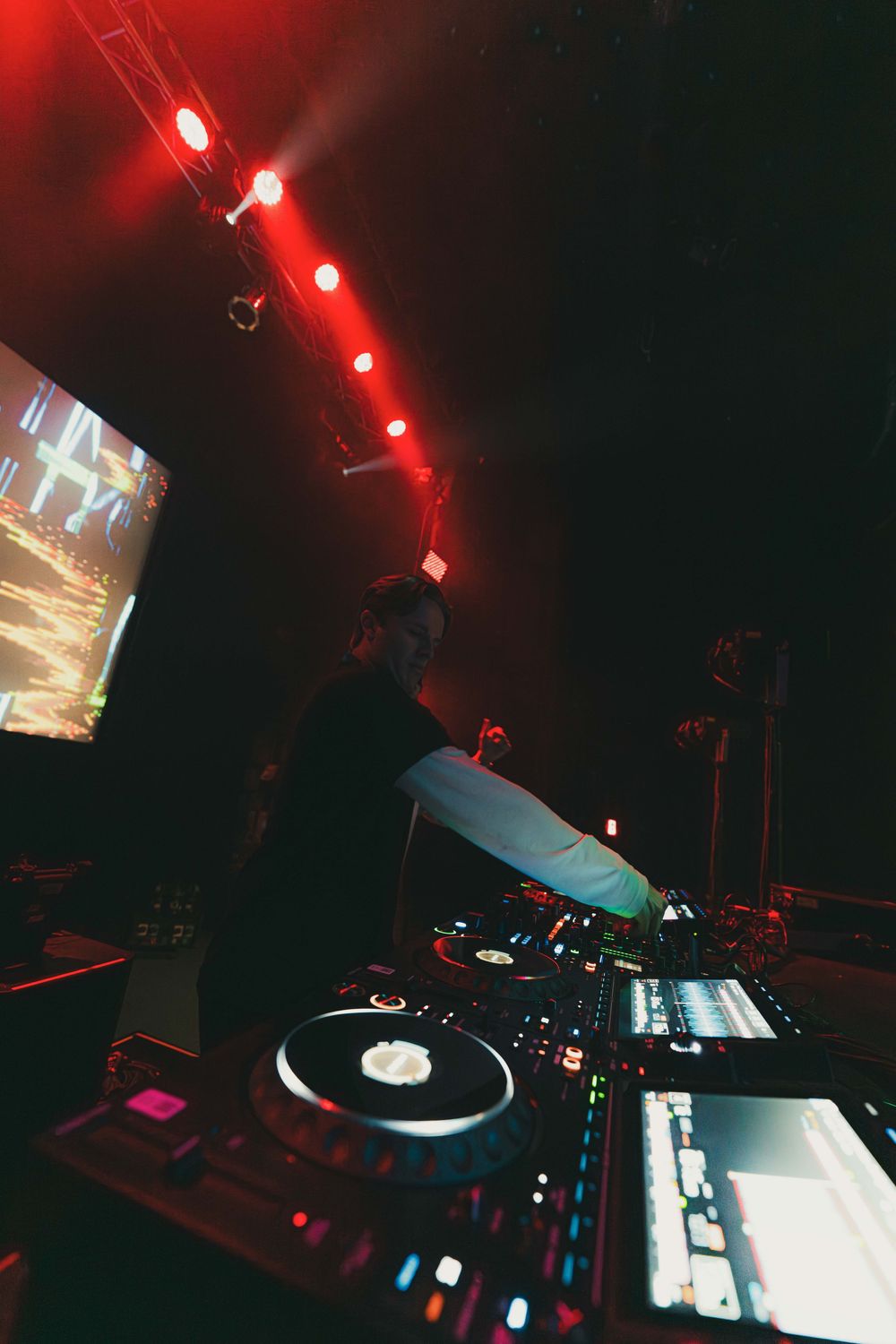 DJ turntable equipment and mixer setup illuminated by red stage lighting at a nightclub performance.