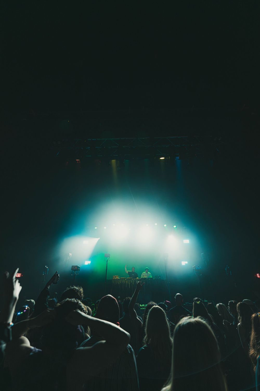 Concert crowd silhouettes against bright stage lights creating atmospheric blue and white glow during live performance.