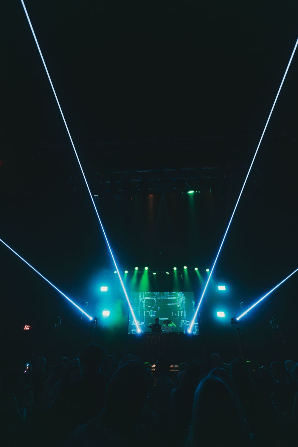 Concert stage illuminated with striking blue laser beams and green accent lights creating a dramatic nighttime atmosphere.