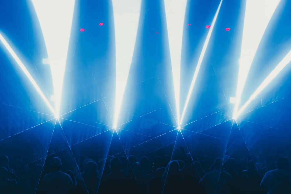 Blue stage spotlights shine bright beams through atmospheric haze during a concert performance.