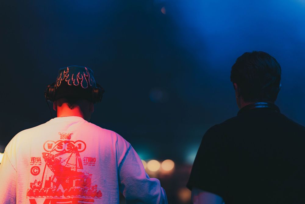 Silhouettes of people in front of vibrant blue and red stage lighting creating an atmospheric concert scene.