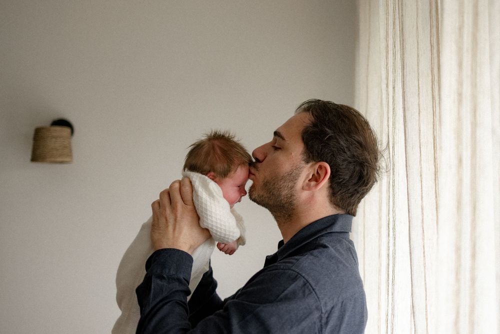 A couple shares an intimate moment while sitting together against a white wall.