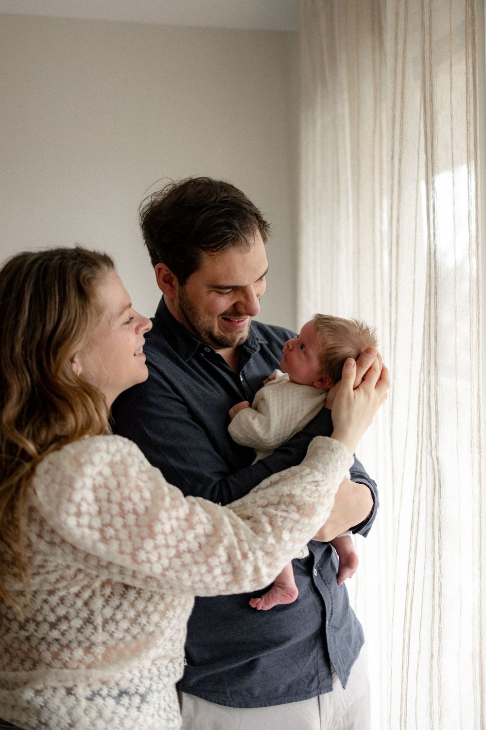 A tender family moment captured in a series of intimate black and white photographs by a window.