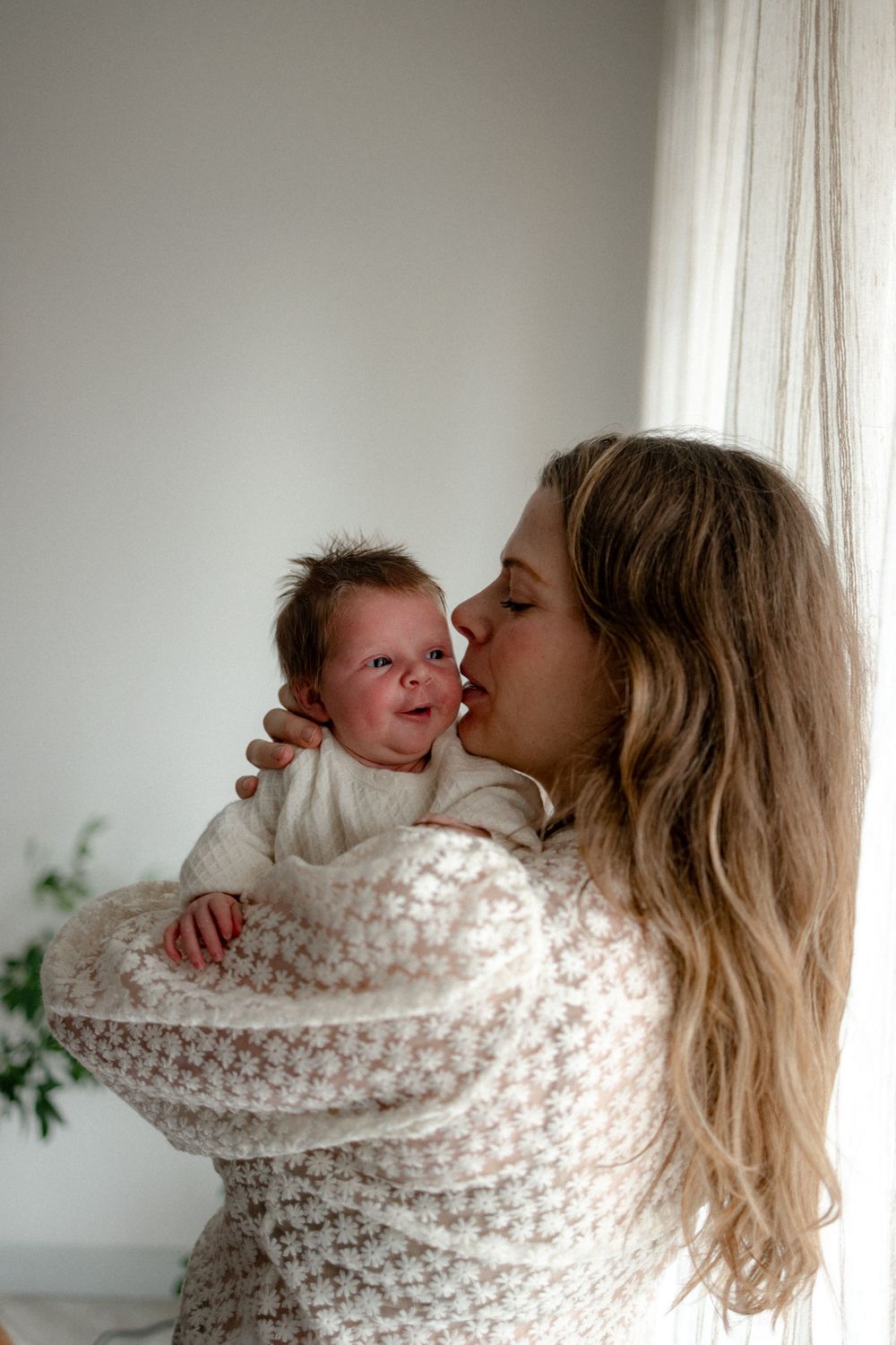 A tender moment between parent and crying newborn baby wrapped in a cozy white knit blanket.