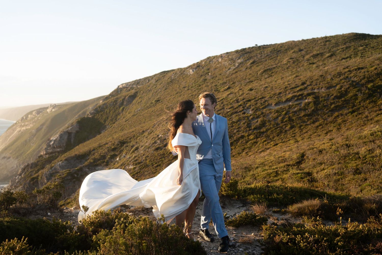 A bride and groom walk together across a grassy hilltop against a cloudy sky in a sequence of motion blur photos.