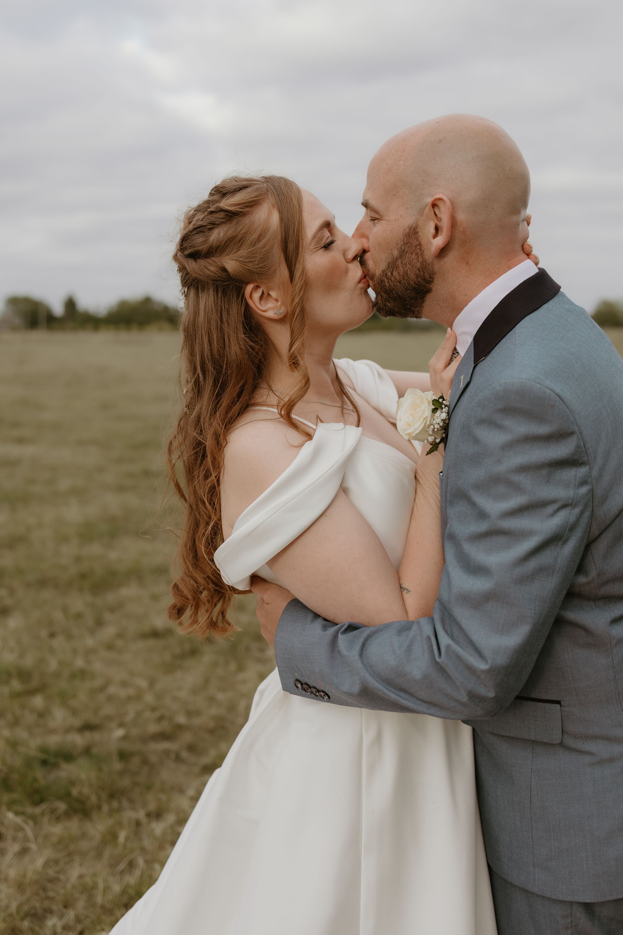 Romantic wedding portrait of Bride and Groom sharing kiss in field.